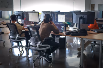 People working on computers in an office with multiple monitors and modern chairs.