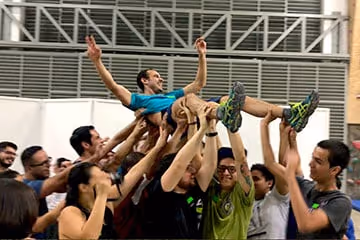 Group of people lifting a smiling man wearing a blue shirt and gray shorts in a celebratory crowd surf.
