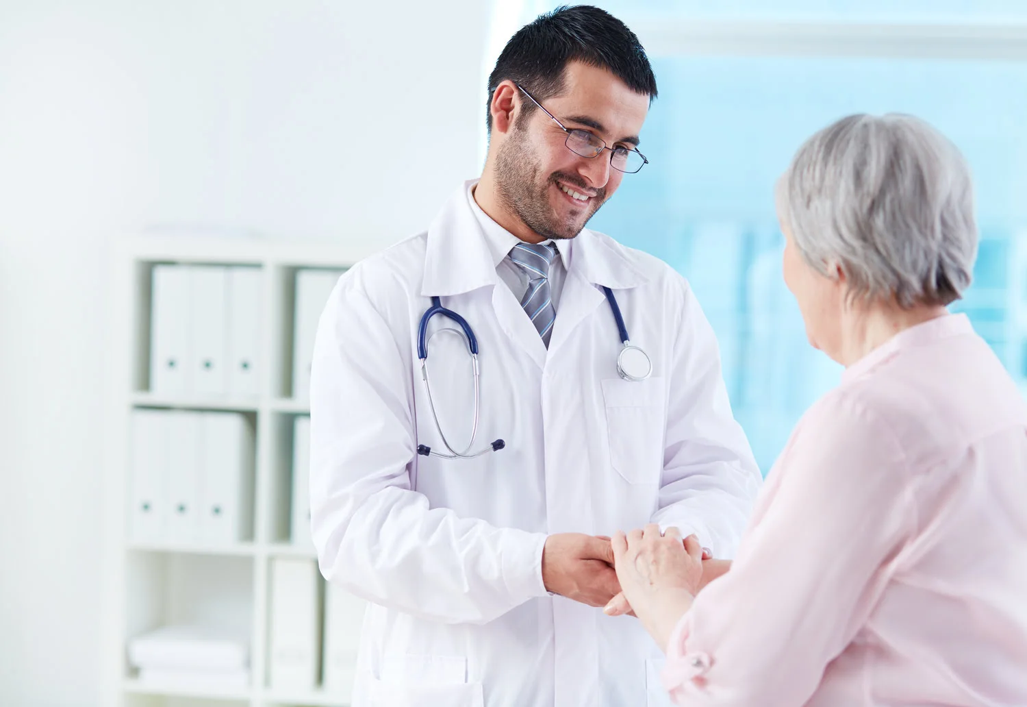 Doctor smiling and holding hand with older woman