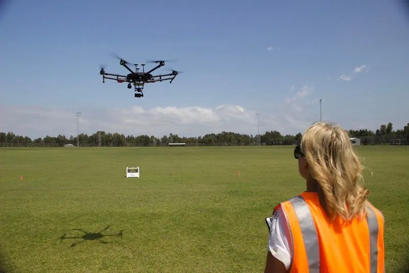 Jackie flying large drone over a park field 