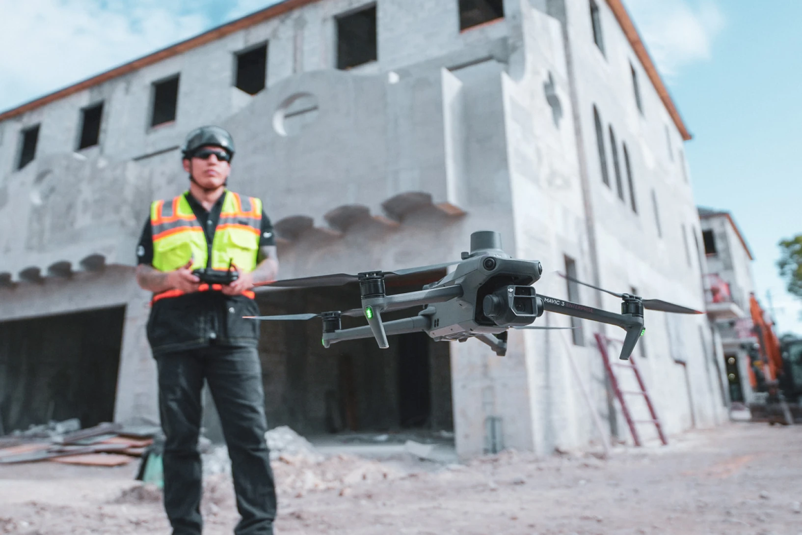 Construction worker operating a DJI Mavic 3 drone in flight on an active jobsite, with a partially built concrete structure in the background.