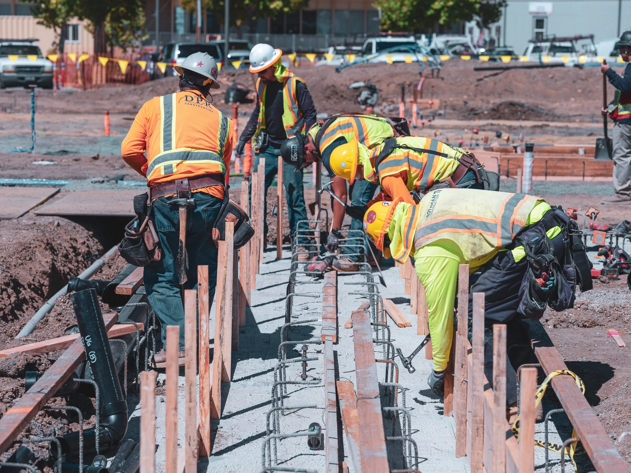 Construction superintendent uses the DroneDeploy mobile app to review a high-resolution drone map on a tablet while standing on an active jobsite, surrounded by steel framework and safety signage.