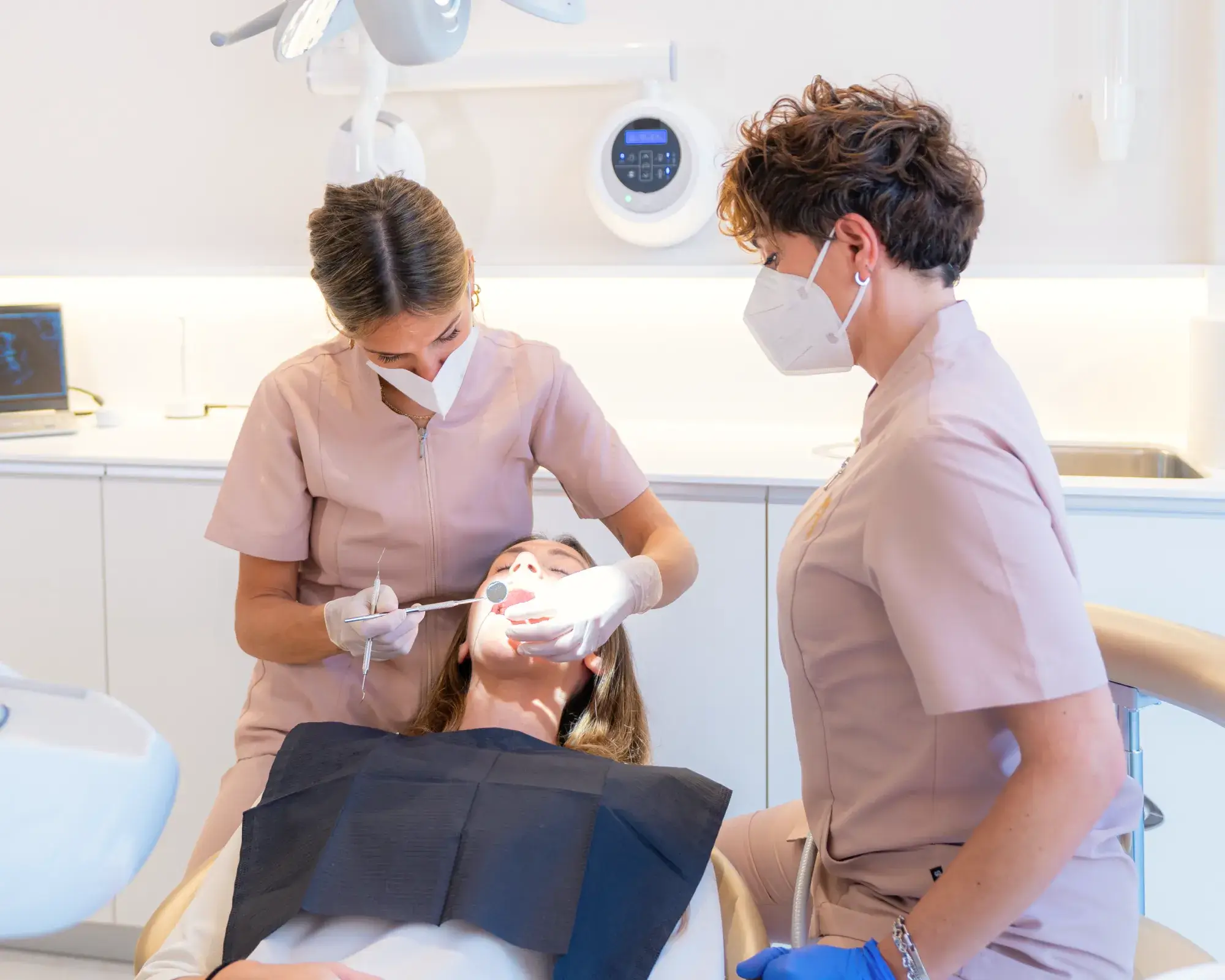 Dentist examining a patient’s mouth while dental assistant looks on in a bright clinic.