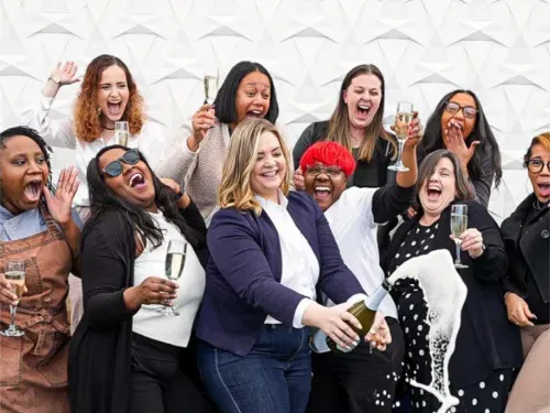 Group of women joyfully celebrating and pouring champagne with glasses raised.