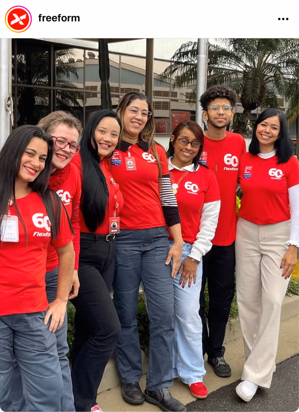 Group wearing matching red shirts posing together outdoors, celebrating with Great Place To Work Certification badges.