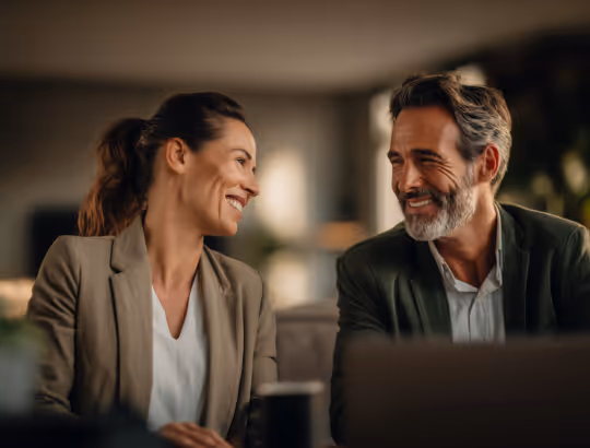 Smiling man and woman in business attire having a friendly conversation during a meeting.