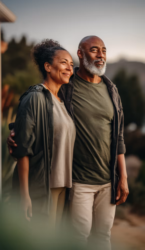 Smiling middle-aged couple standing outdoors with arms around each other, looking into the distance.