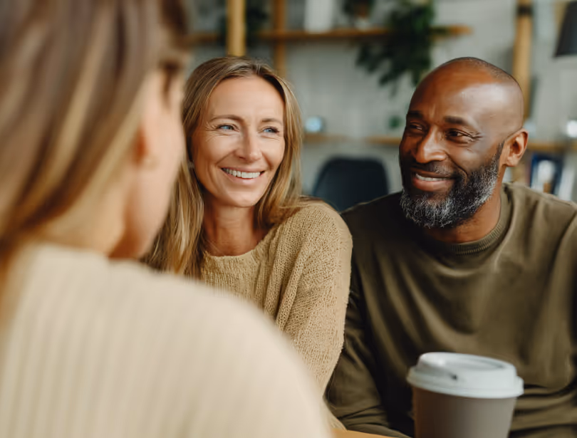 Smiling middle-aged couple sitting close together at a table during a conversation, with warm indoor lighting.