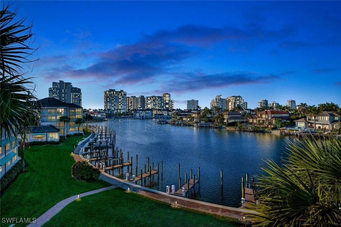 Waterfront residential area with docks, green lawns, palm trees, and high-rise buildings at dusk.