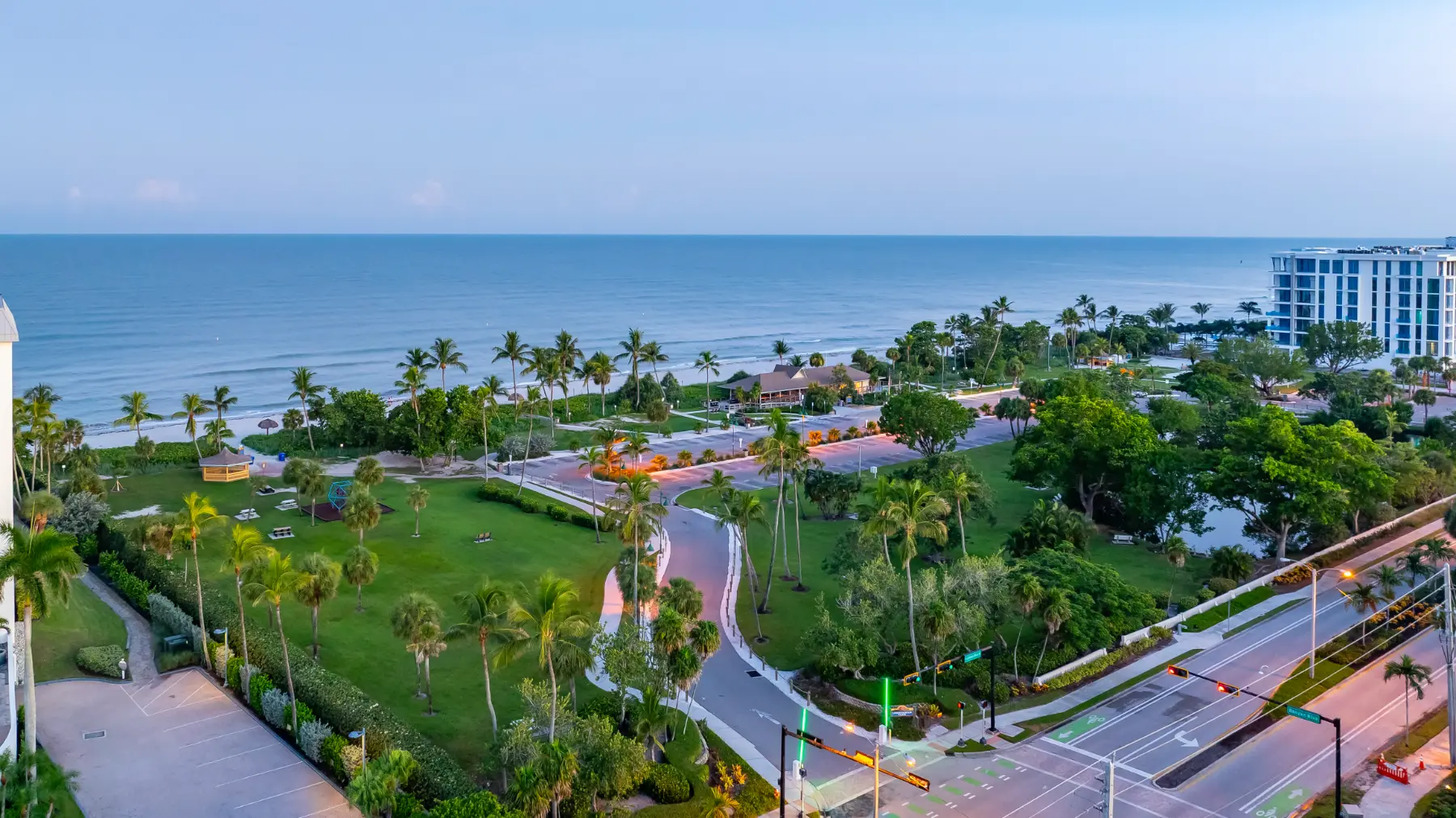 Naples, Florida oceanfront backyard with pool, lounge chairs, palm trees, and green lawn under a clear sky.