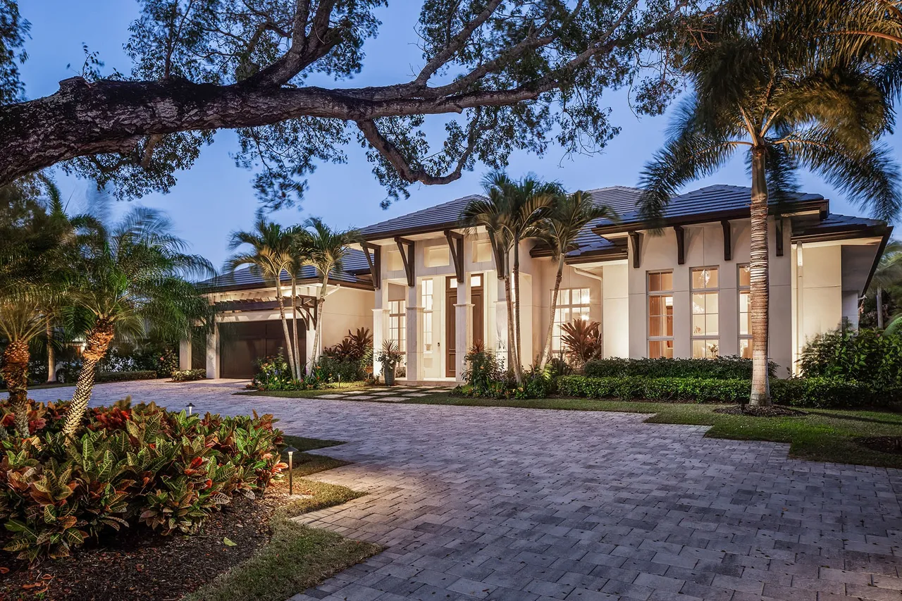 Modern house exterior at dusk with illuminated pool, hot tub, outdoor fireplace, and patio seating.