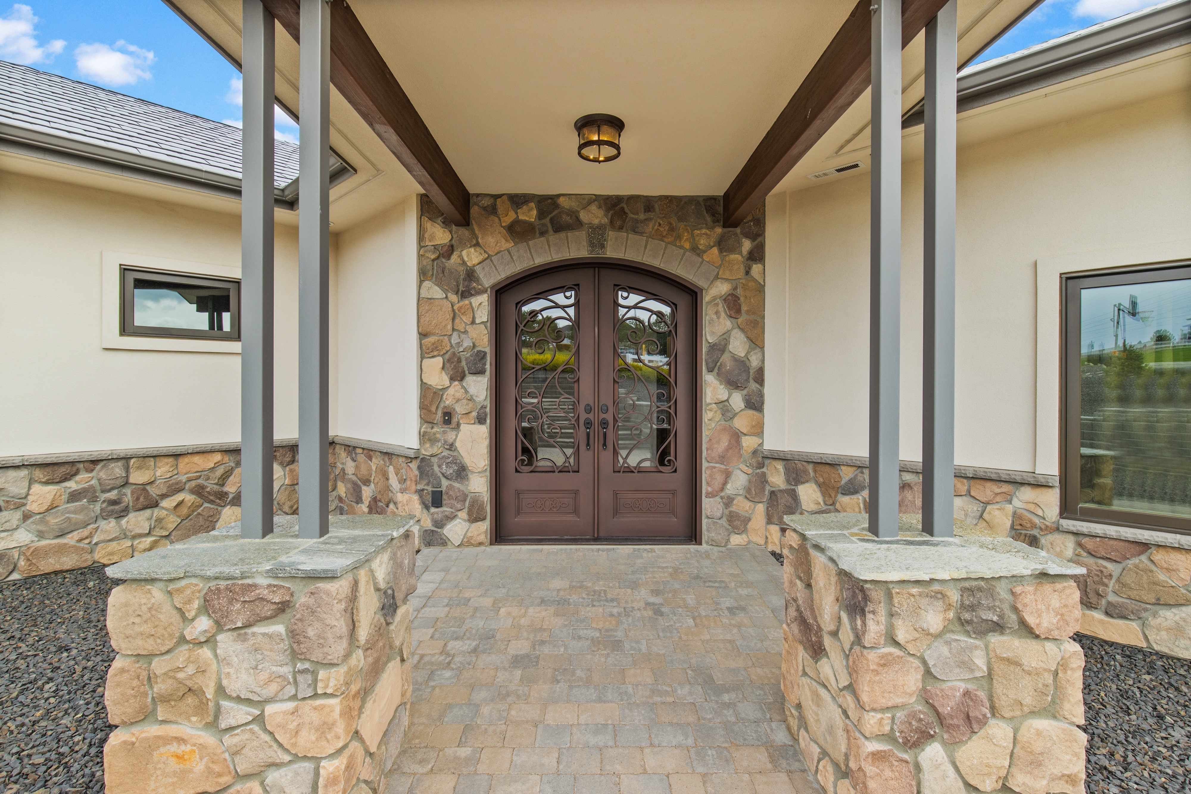 Stone-covered porch entrance with double wooden doors featuring glass panels and decorative wrought iron details.