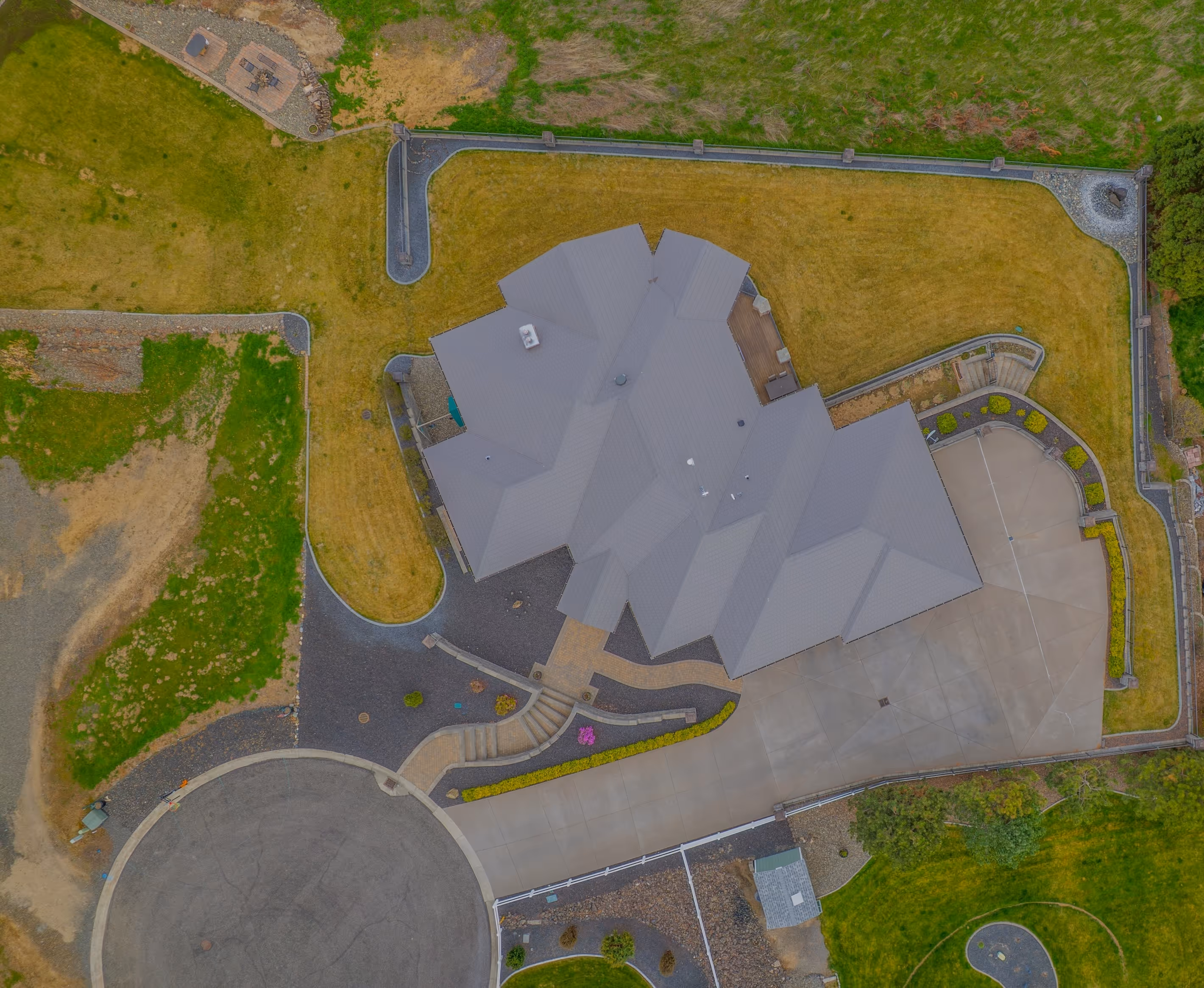 Aerial view of a large house with grey roof, surrounding lawn, driveway, and a cul-de-sac.