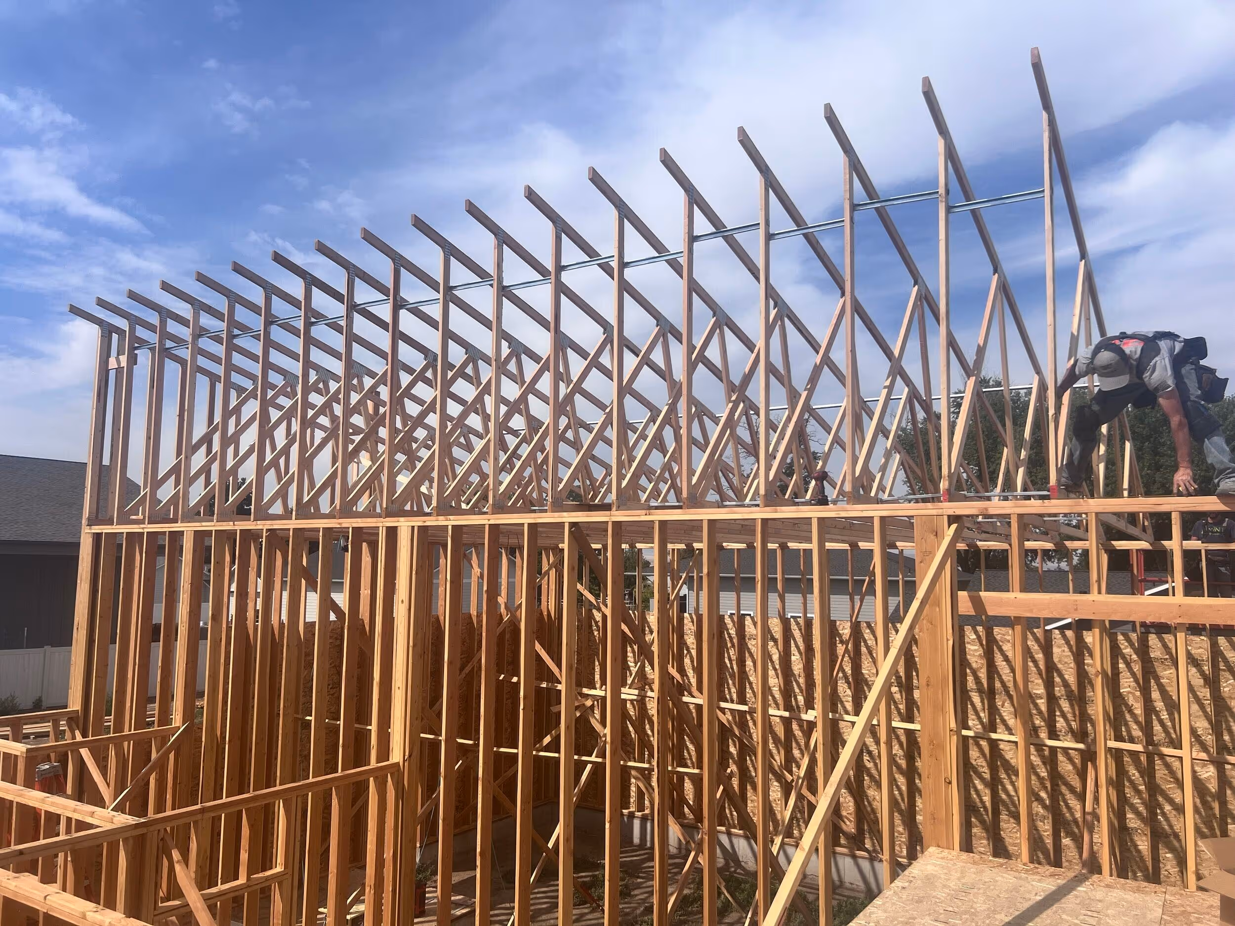 Wooden framework of a house under construction with a worker positioning beams on top.