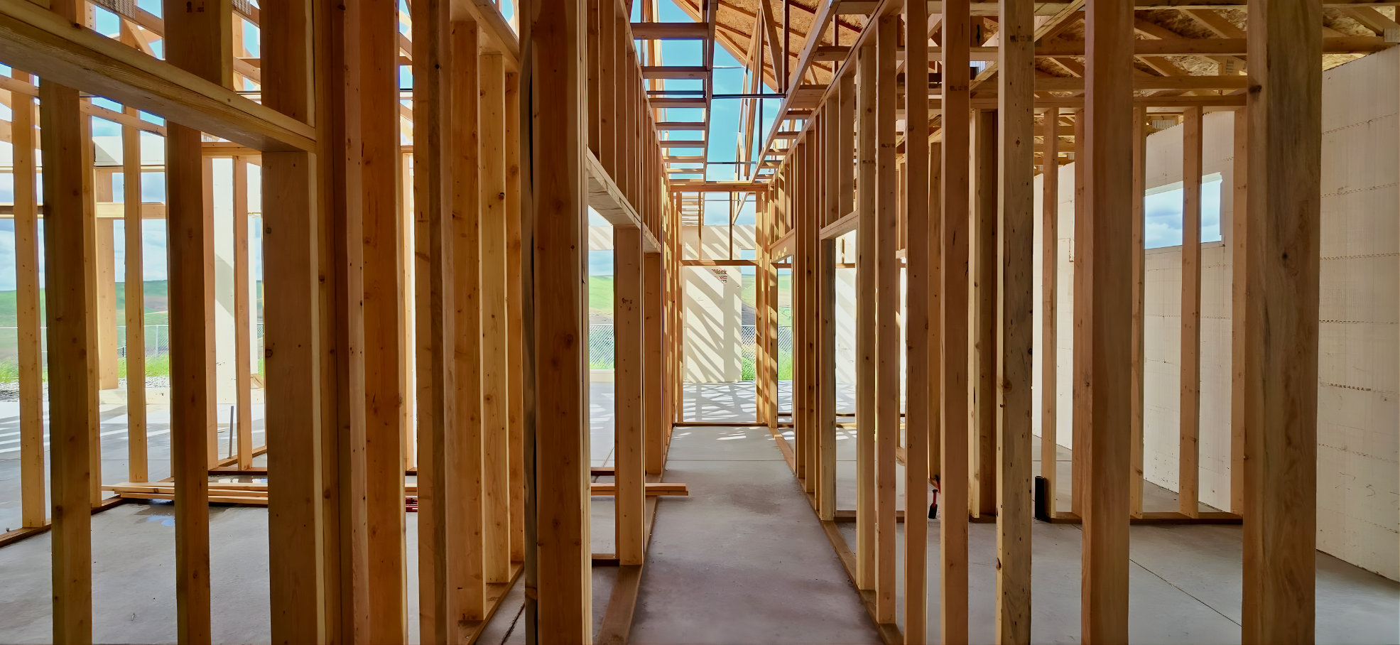 Interior view of a house under construction showing wooden framing and concrete floor with natural light.