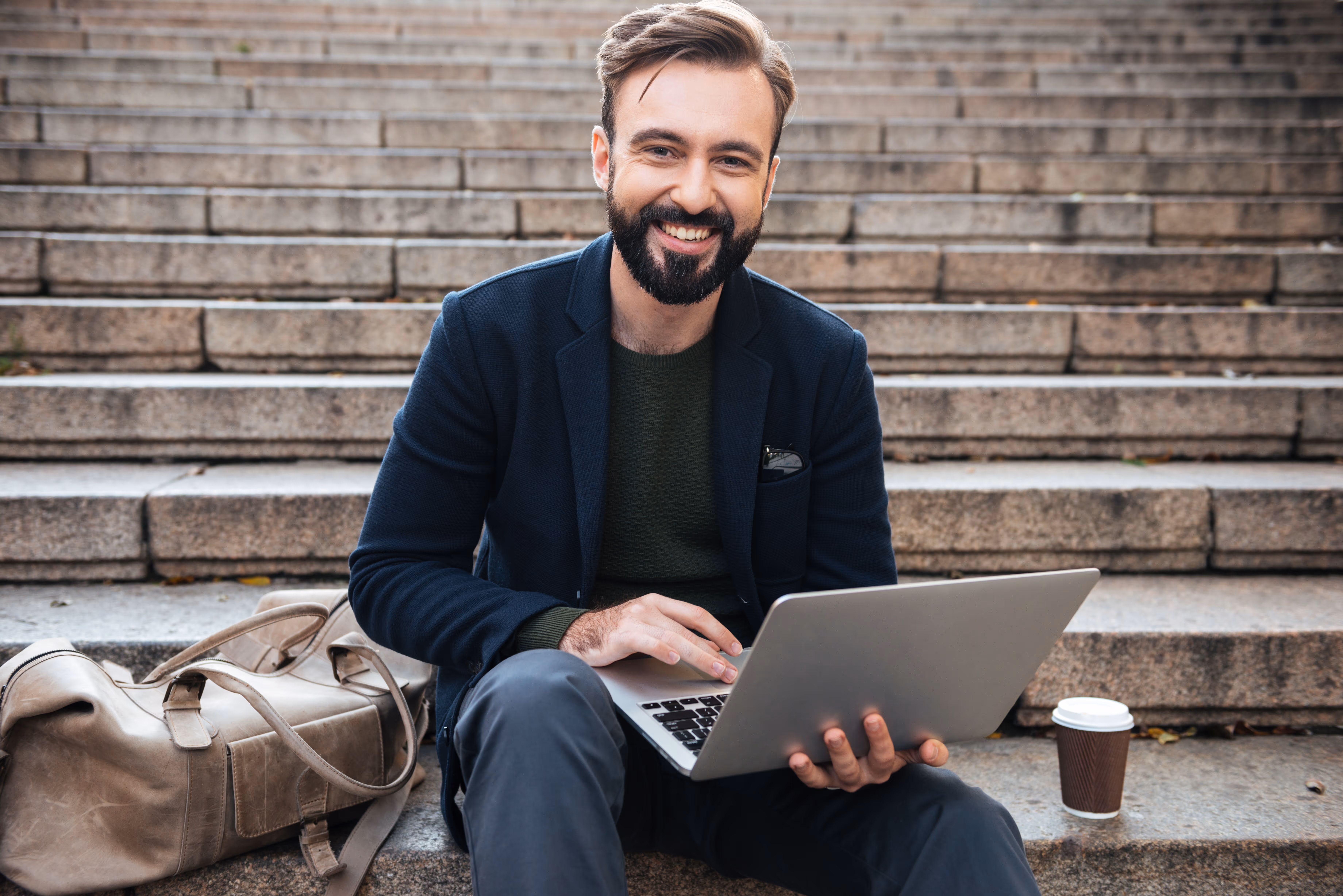 Mann mit Laptop auf einer Treppe, lächelnd