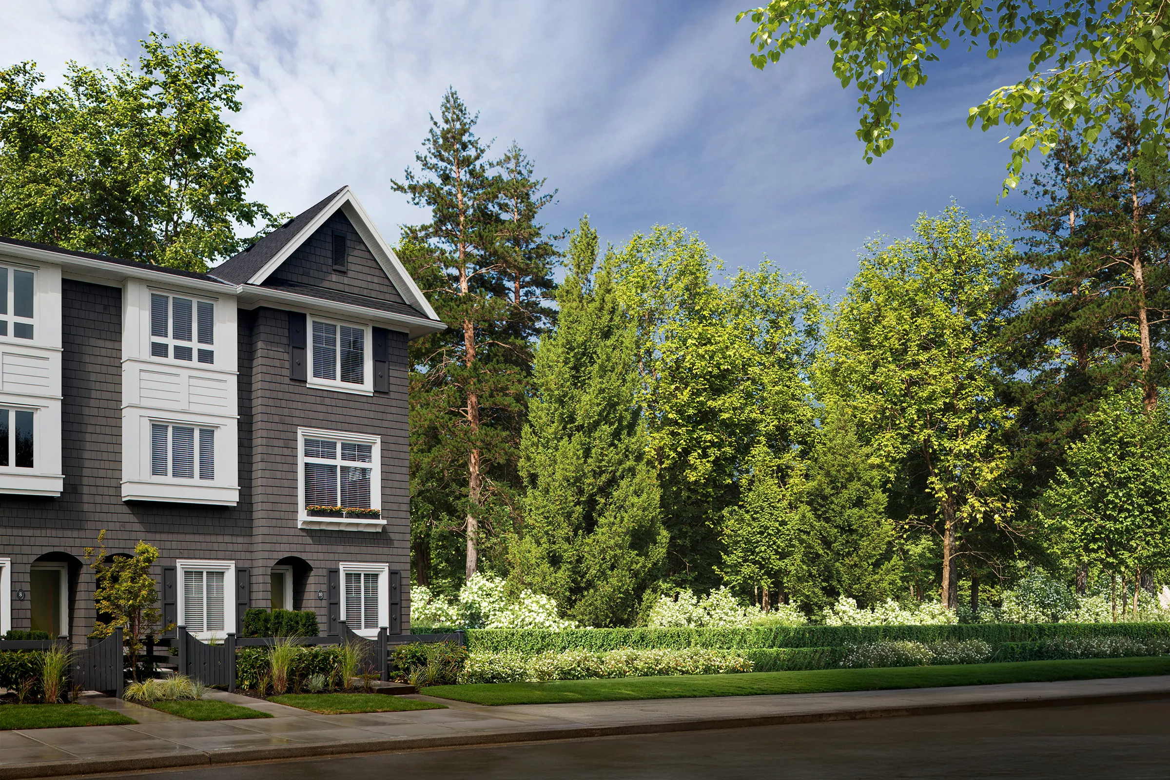 Row of grey QUEENS townhomes with white trim beside a green lawn and tall trees in Bear Creek, Surrey