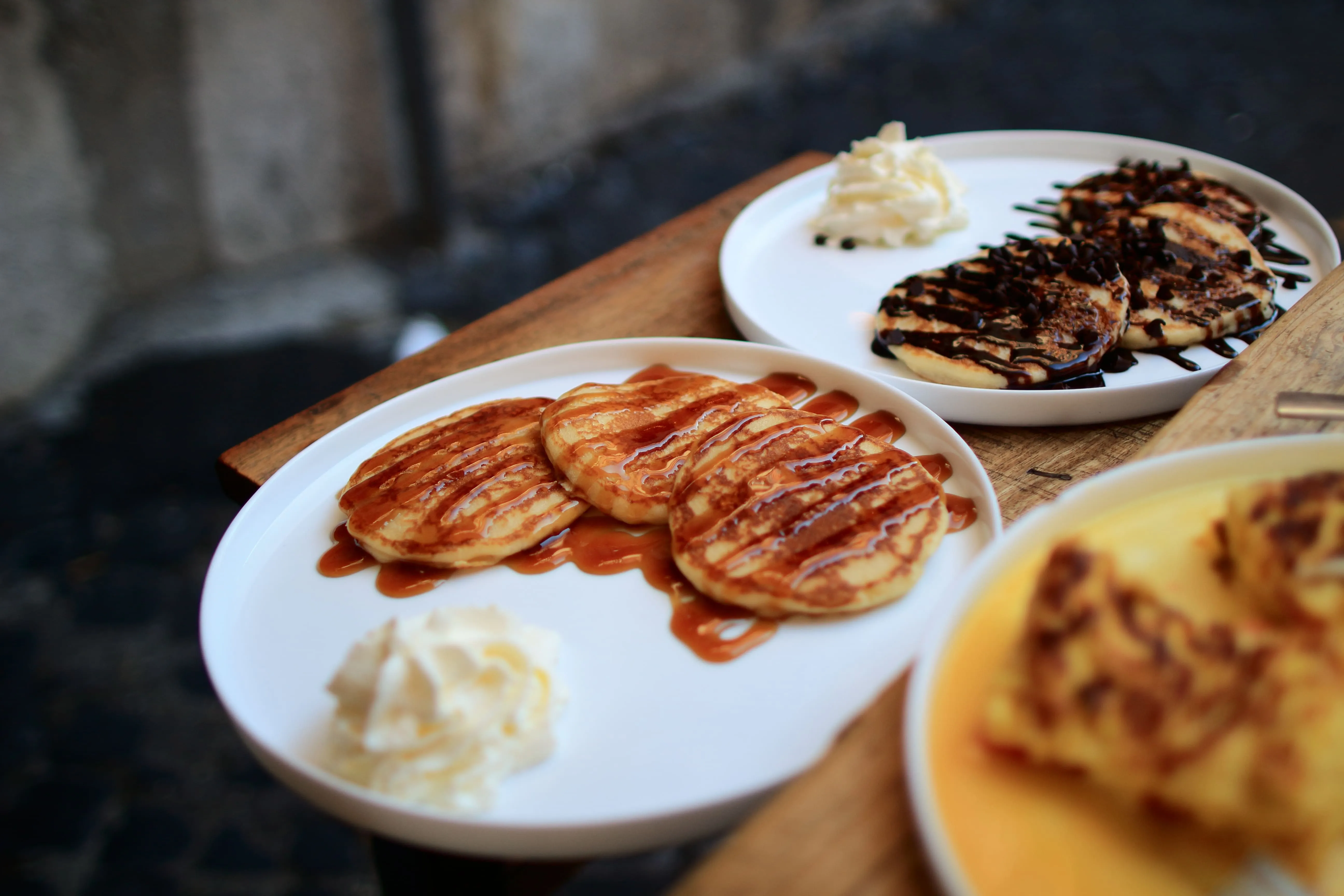 Three pancakes drizzled with caramel sauce and whipped cream on a white plate on wooden table.