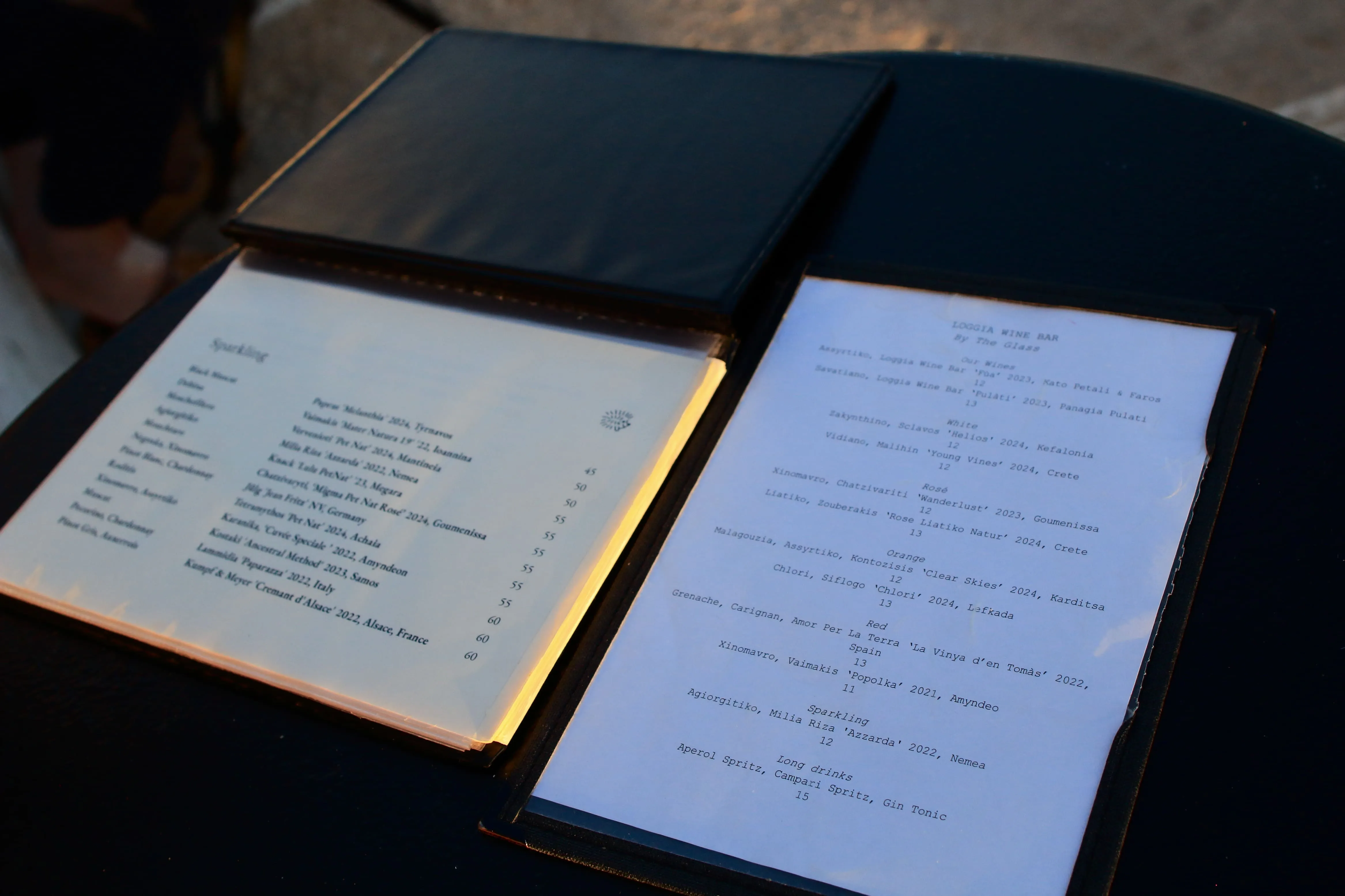 Two open menus on a dark round table showing wine and drink listings at Loggia Wine Bar.