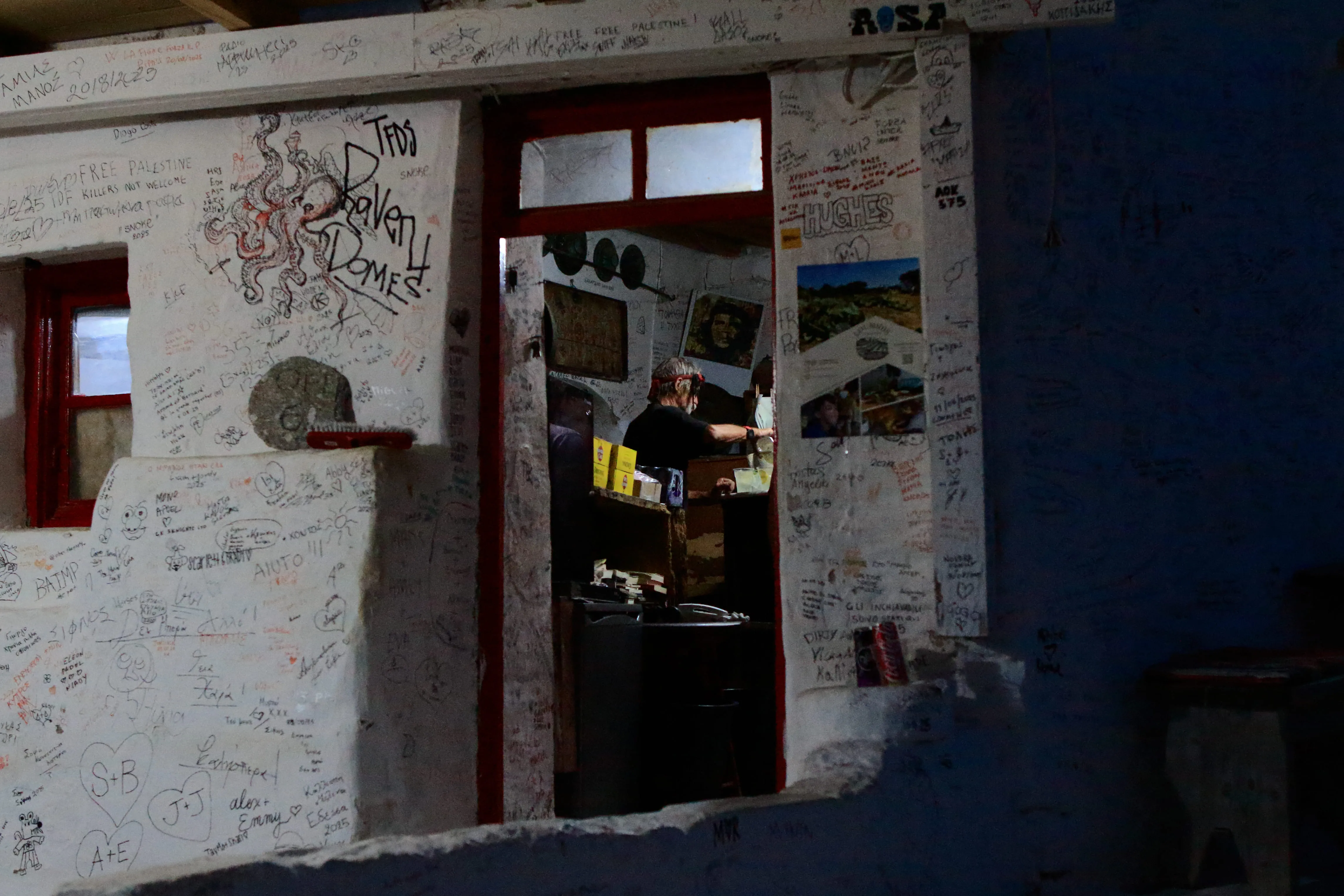 Dimly lit room with walls covered in graffiti and a person inside pouring a drink.
