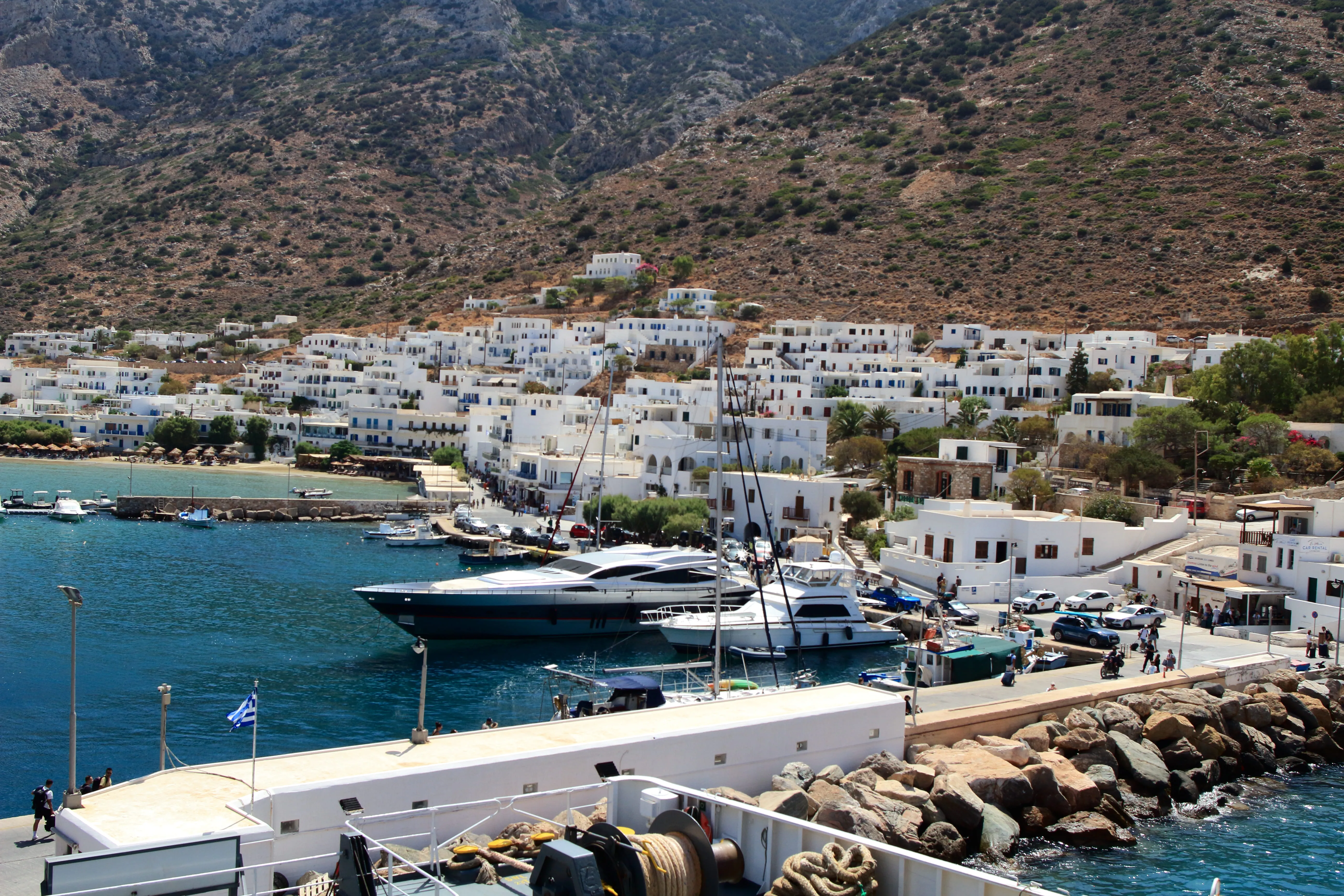 Harbor with yachts, white buildings, and rocky hills in a sunny coastal village.