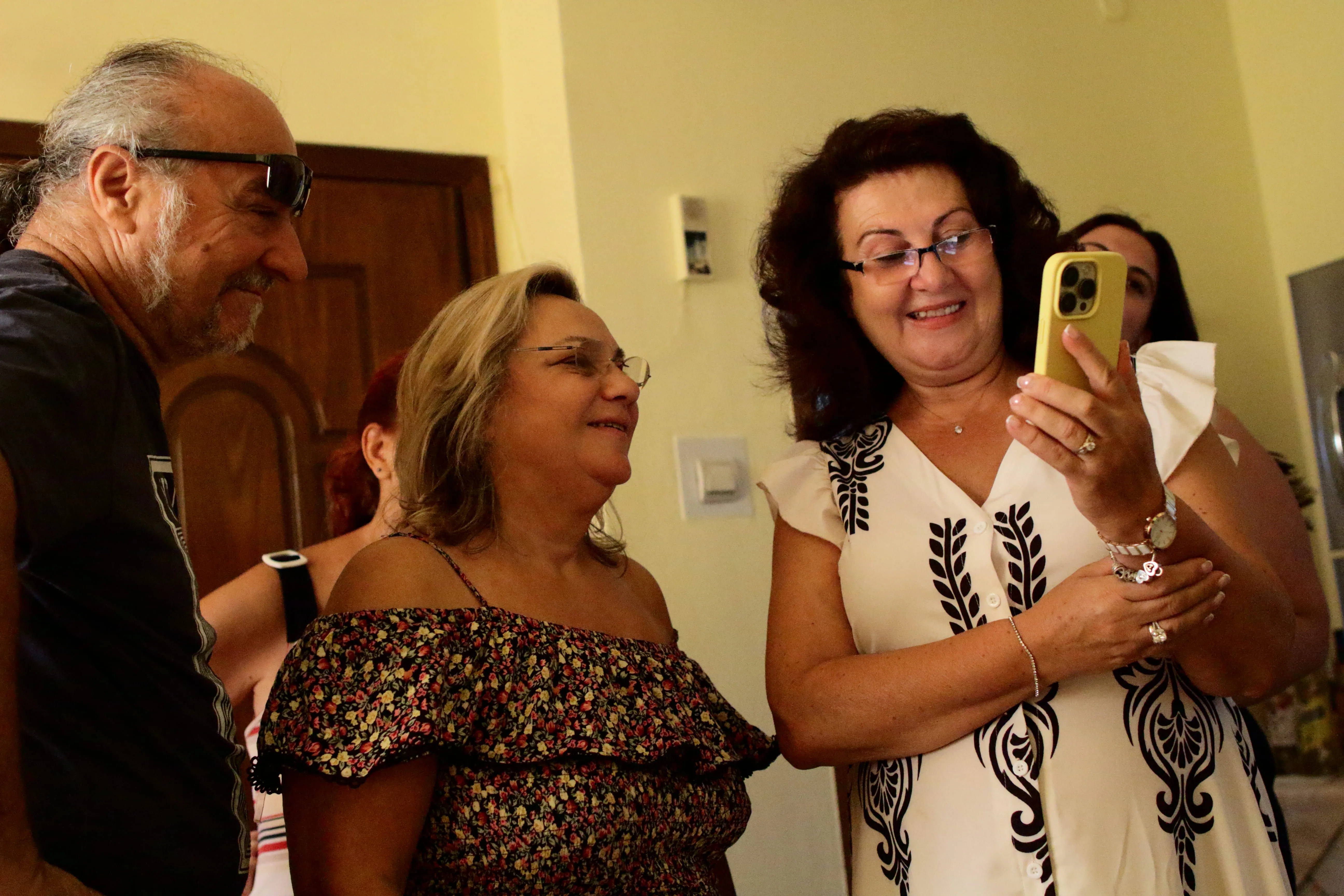 Group of smiling adults looking at a smartphone indoors with light walls and a wooden door.