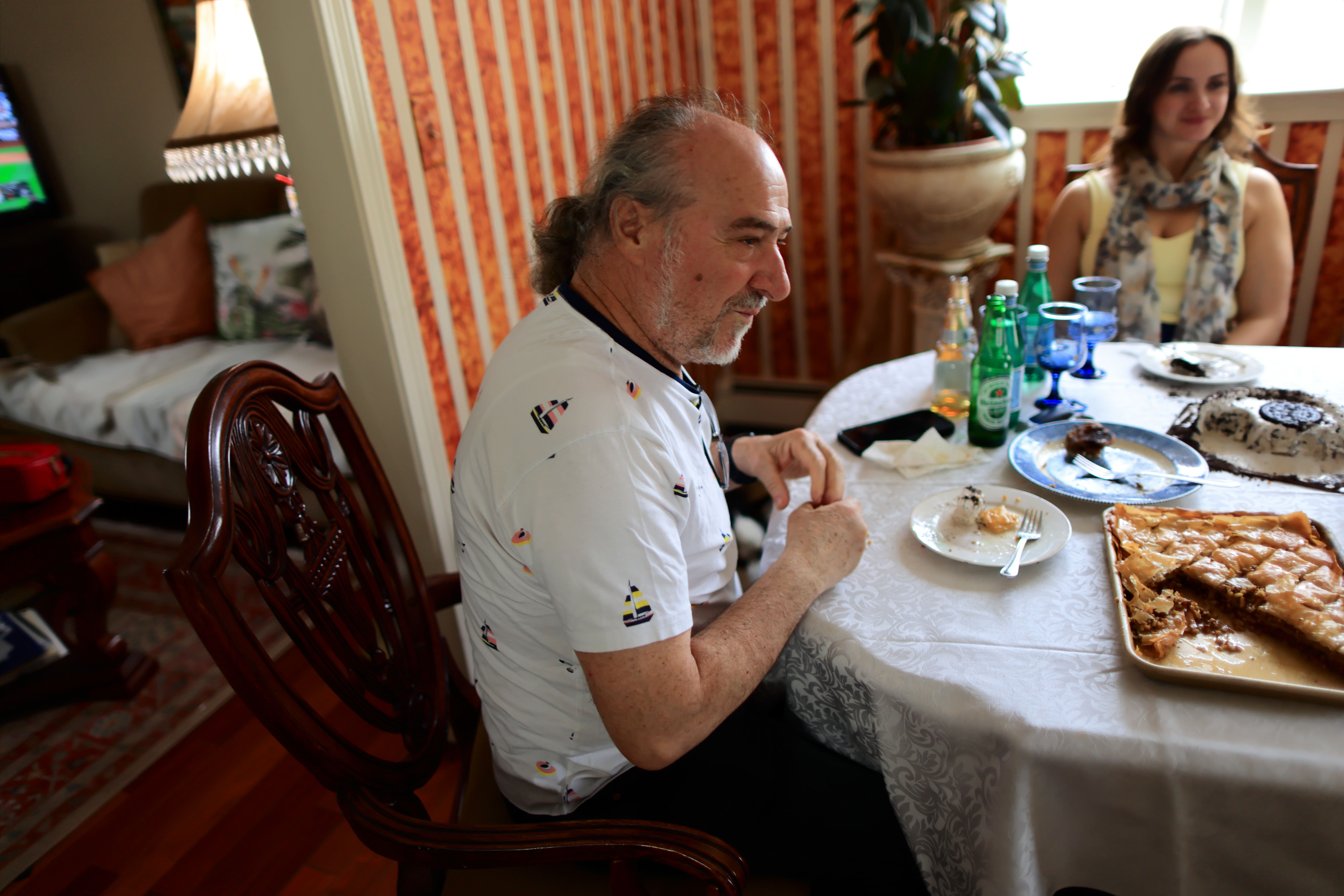 Man in white shirt sitting at table with woman, plates of food, drinks, and desserts.