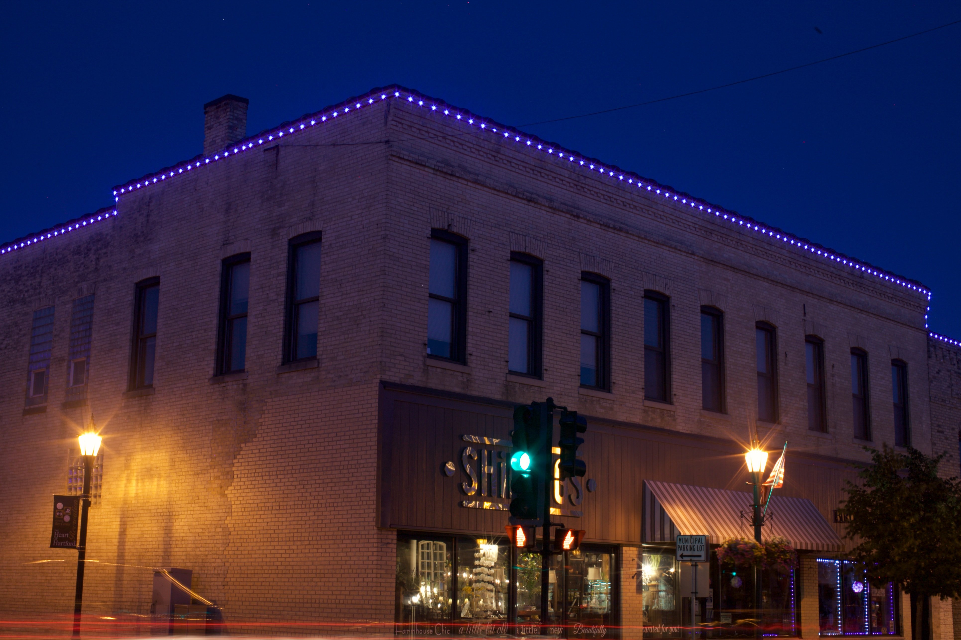 Commercial brick building at night featuring custom purple roofline string lighting and illuminated storefront.   