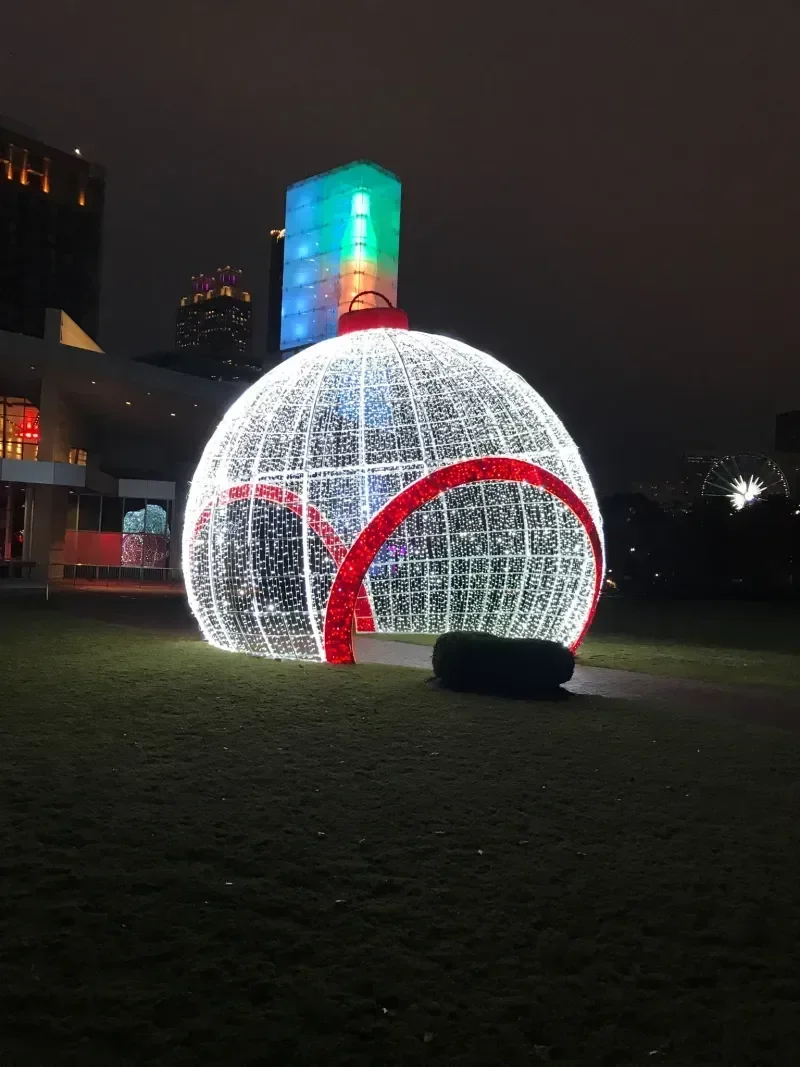 Large illuminated Christmas ornament decoration with red and white lights on grass at night.