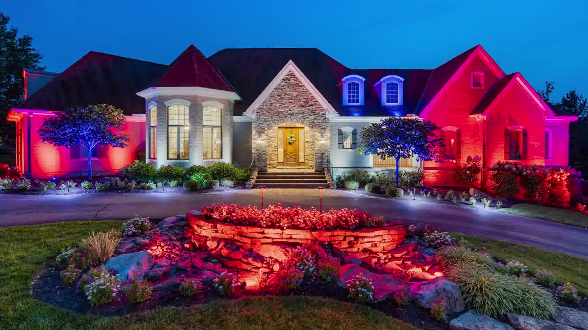 Luxury house at dusk with colorful red and blue exterior lighting and landscaped front garden.