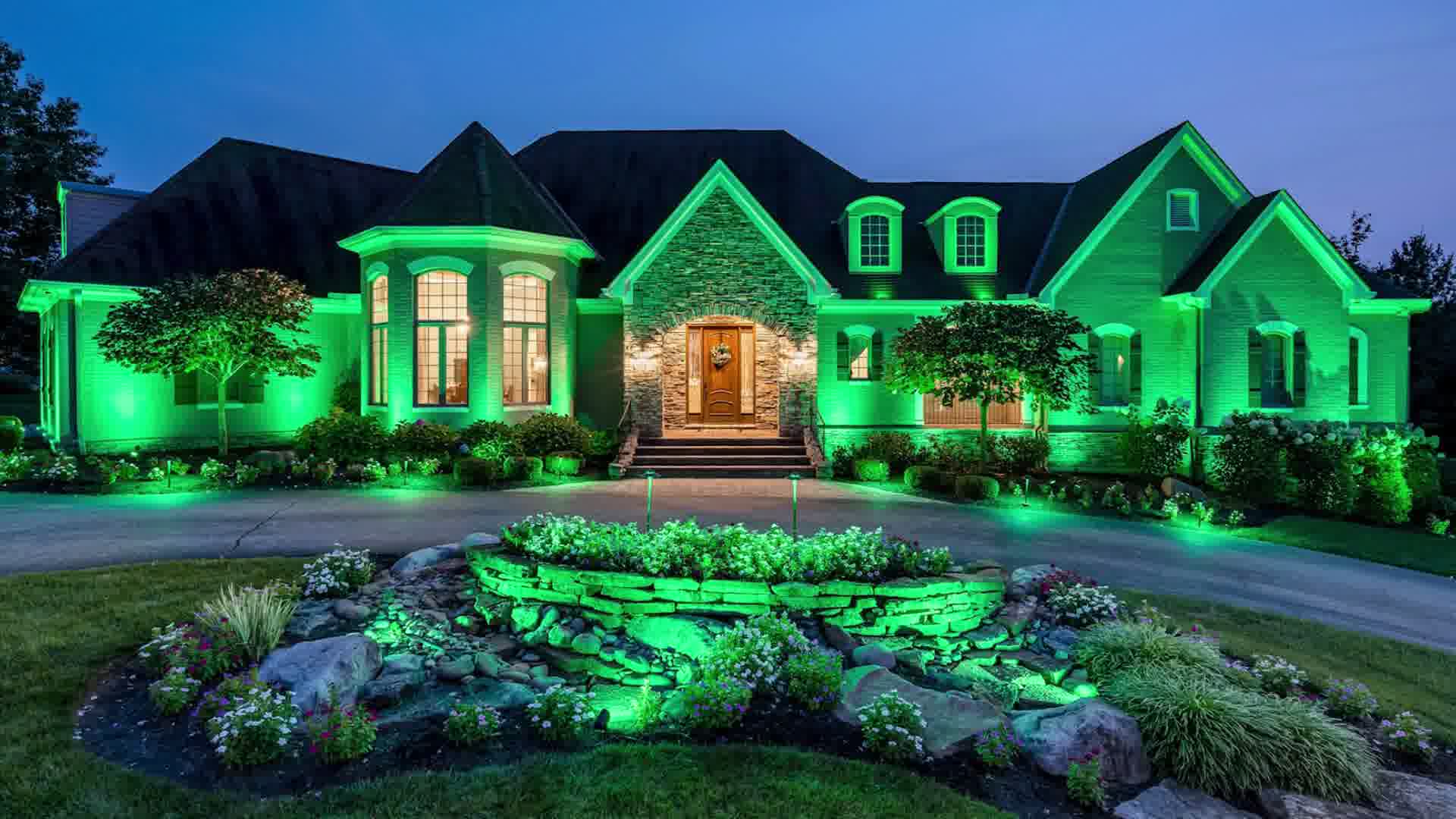 Large house at dusk with green landscape lighting illuminating the garden and exterior walls.