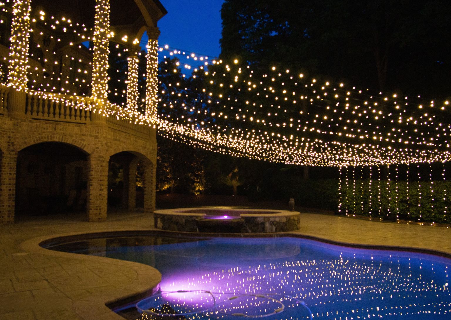 Warm outdoor lighting installation on a residential home exterior at dusk, featuring glowing LED lights that enhance landscaping and architectural elements. The professional lighting design creates a welcoming atmosphere and highlights outdoor spaces for enhanced curb appeal.
