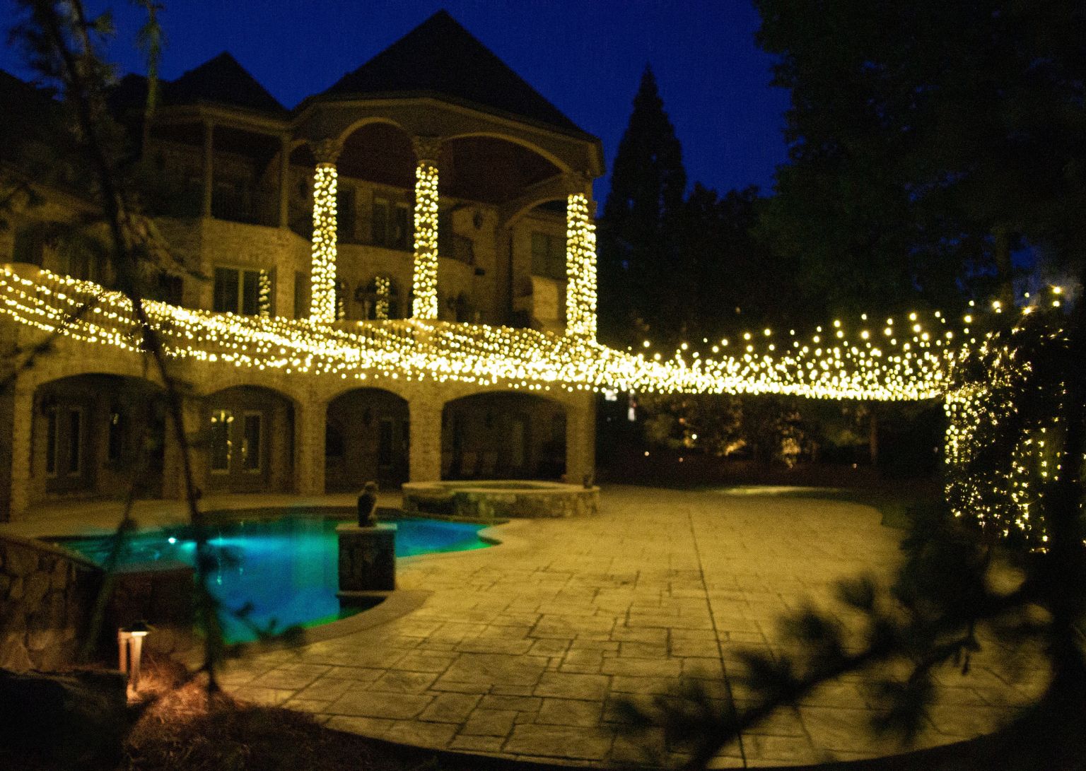 Warm outdoor lighting installation on a residential home exterior at dusk, featuring glowing LED lights that enhance landscaping and architectural elements. The professional lighting design creates a welcoming atmosphere and highlights outdoor spaces for enhanced curb appeal.