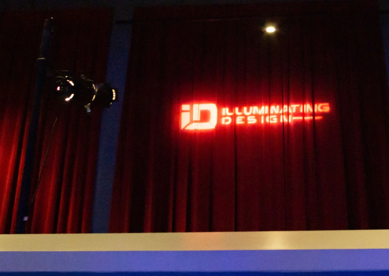 Red stage curtain with spotlight projecting the words Illuminating Design and a logo.