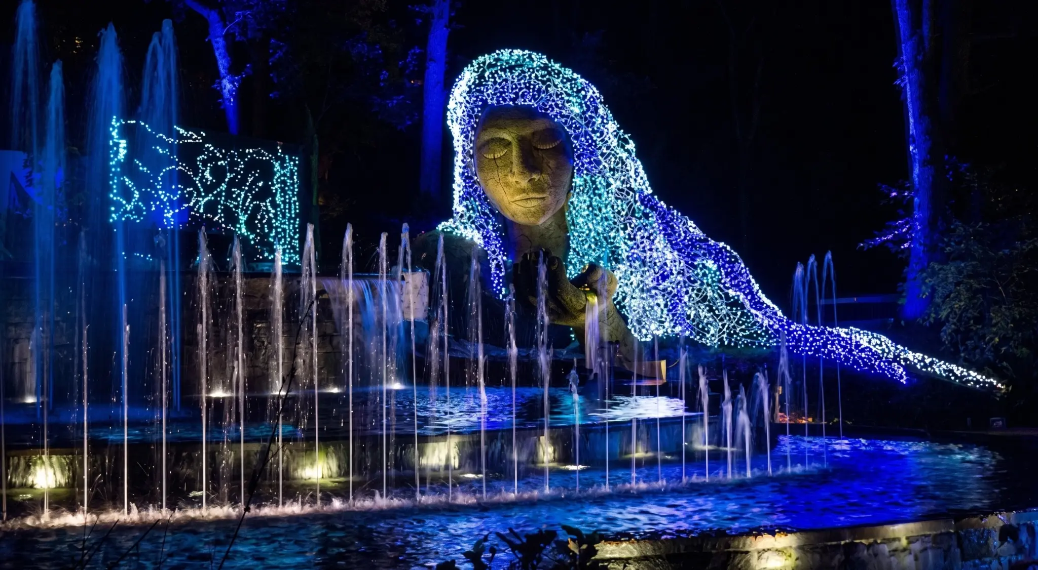 Professional event lighting installation with vibrant blue water fountains and a LED light-covered sculpture.