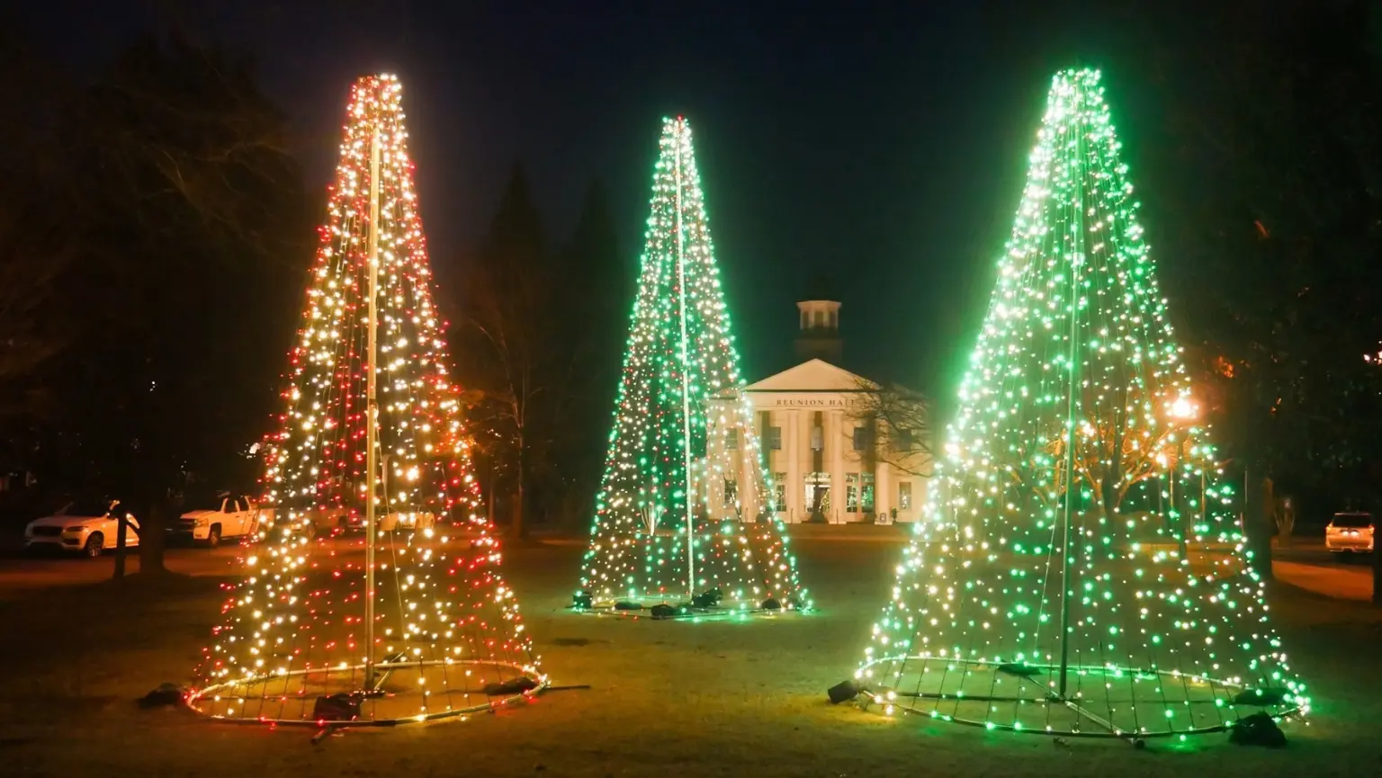 Large outdoor illuminated red and green cone light trees in front of a venue building.