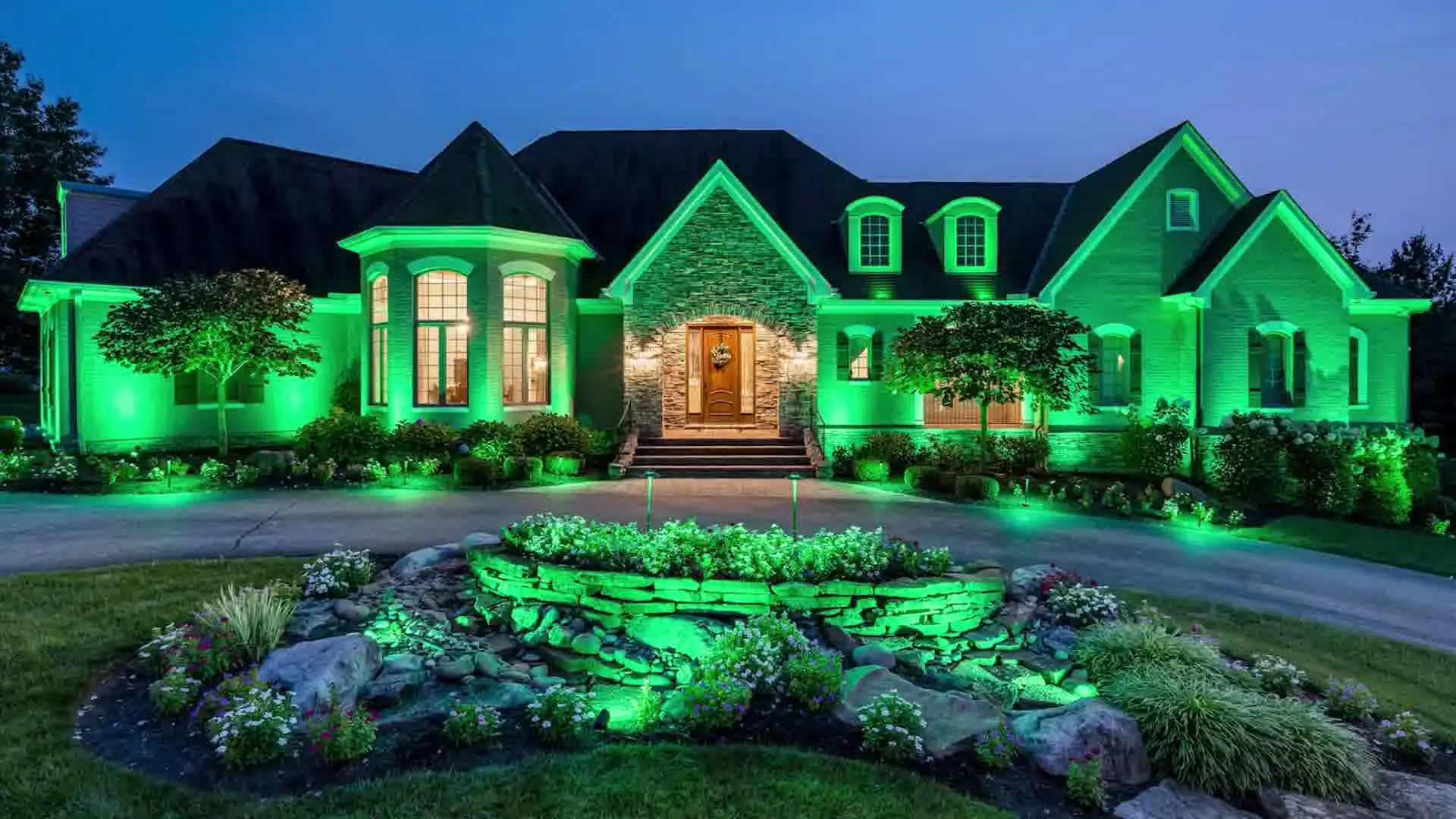 Luxury home exterior illuminated with vibrant green LED landscape lighting and outdoor flower bed illumination.