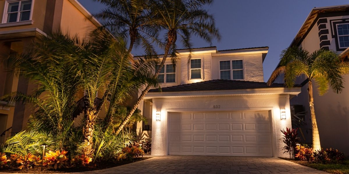 Beautiful home exterior illuminated with uplighting, highlighting the architecture, landscaping, and palm trees, demonstrating the impact of uplighting design on curb appeal at night.