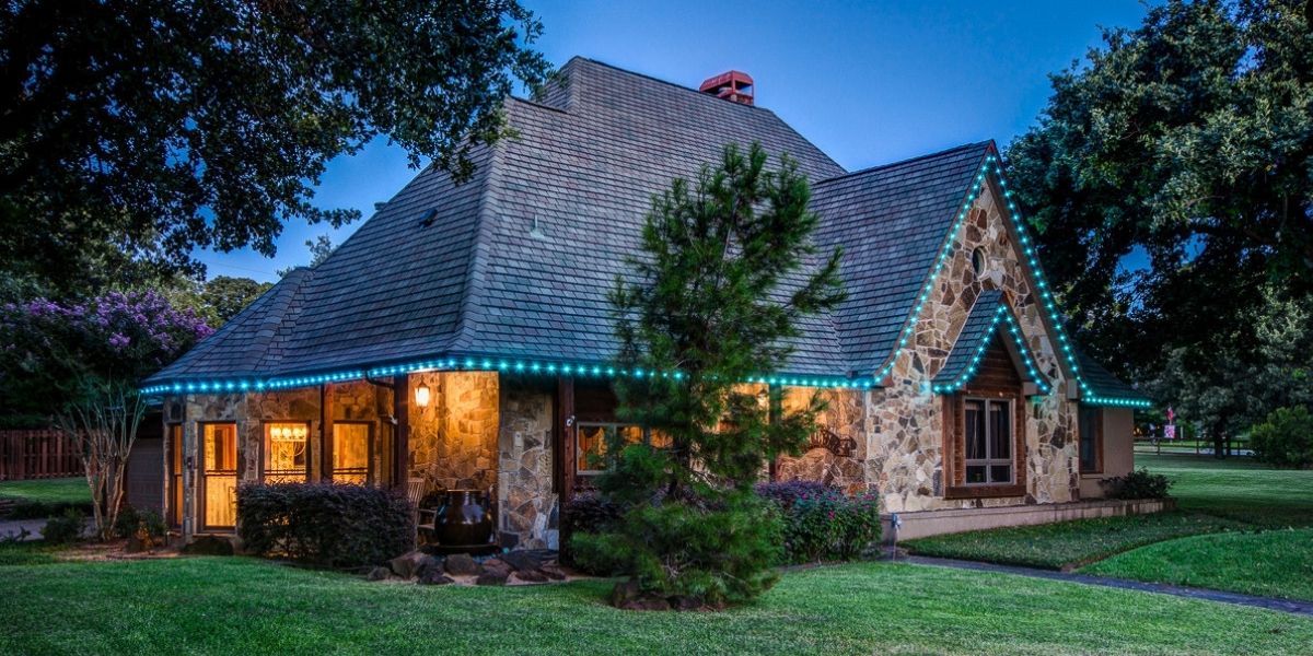 user-inserted Stone house with permanent trim lighting installed along roofline and eaves, showcasing vibrant blue LED accent lighting for enhanced nighttime curb appeal and outdoor aesthetics.