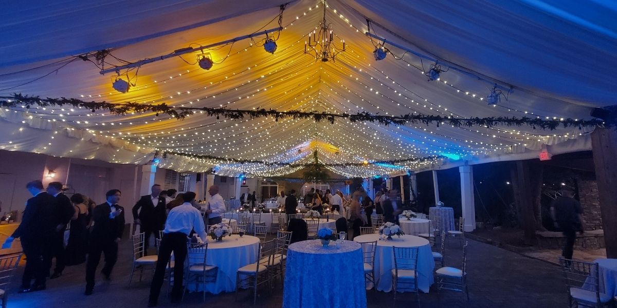 Elegant outdoor wedding reception under a tent with professional uplighting, string lights, and ambient event lighting creating a warm atmosphere for guests and celebrations.