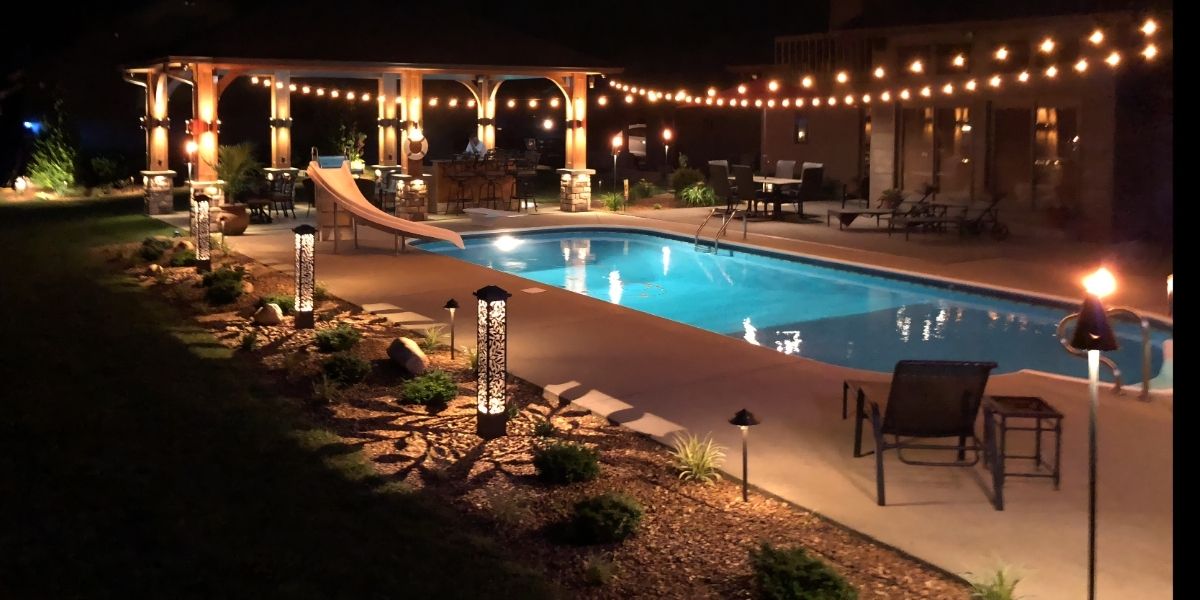 Luxury backyard pool area with landscape uplighting, pathway lights, and warm outdoor event lighting creating an elegant atmosphere for residential gatherings and evening entertainment.