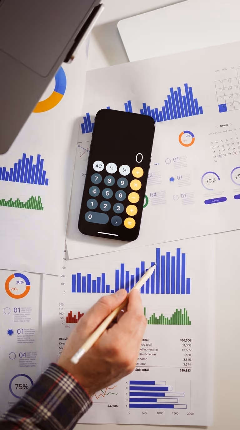 Smartphone calculator and printed bar charts used for manual budget tracking, representing Earthmaster's legacy project tracking system where spend alerts and reporting required manual effort instead of configurable notifications in Matidor.