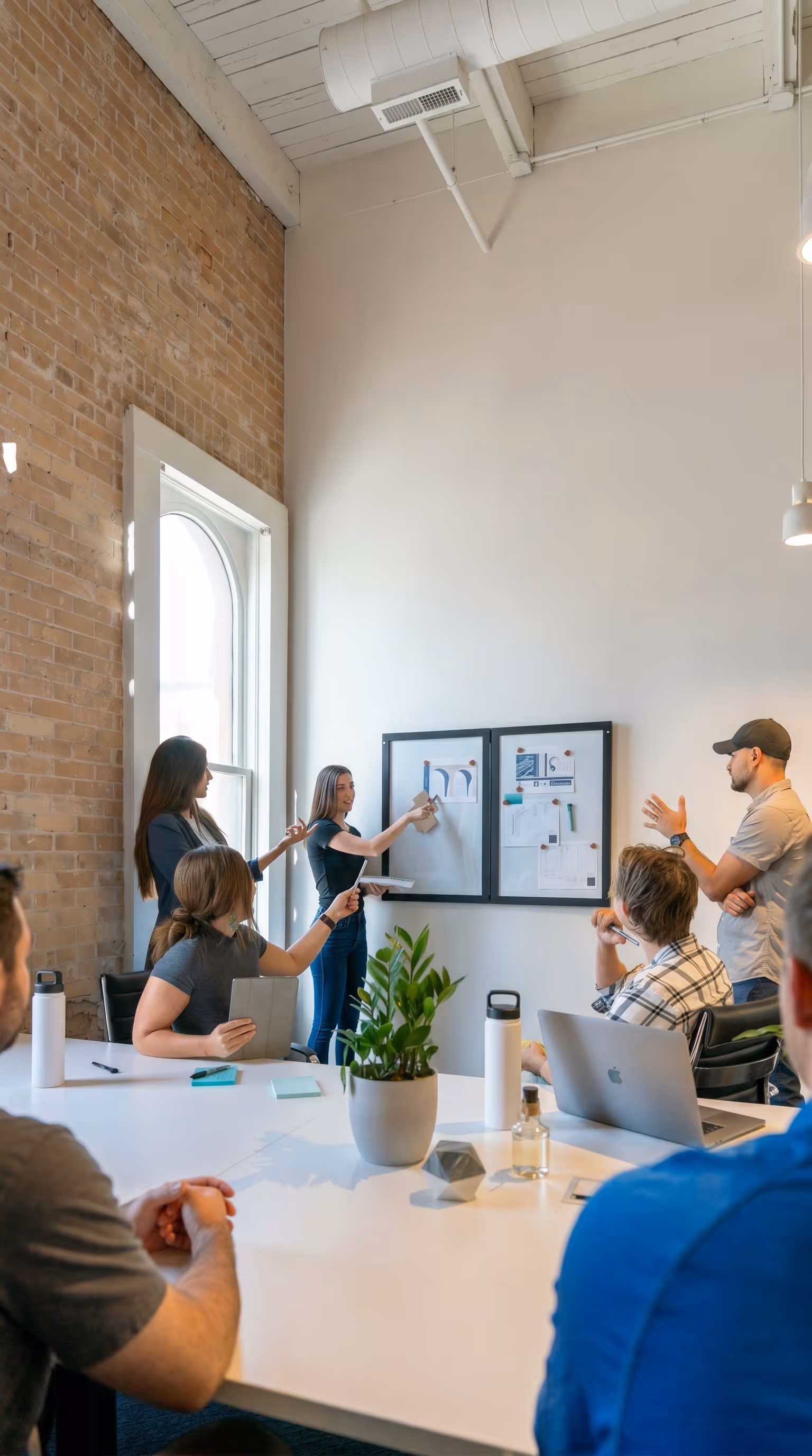 A small team collaborating in a bright modern office with exposed brick walls, gathered around a pinboard displaying project materials, representing the improved team coordination and stakeholder communication Project Forest achieved after adopting Matidor, including faster reporting and 10x more efficient project handling.