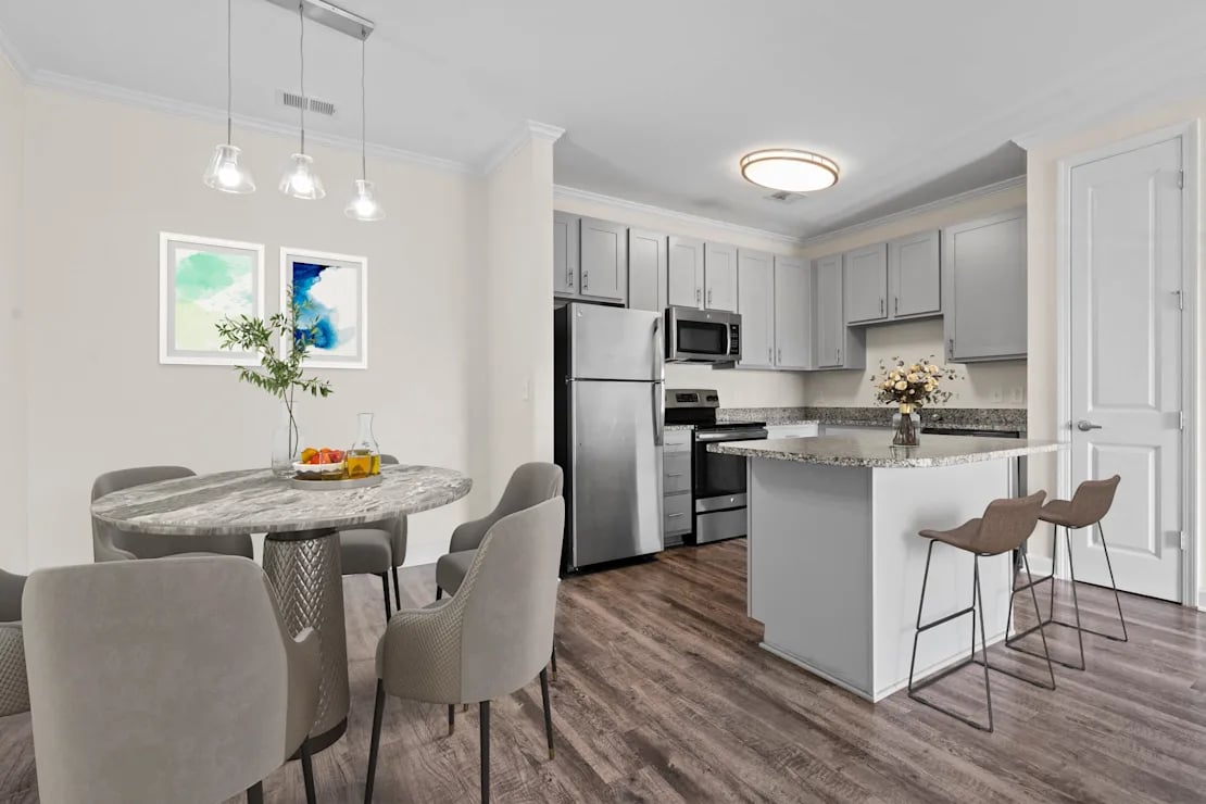 Modern kitchen with stainless steel appliances, a granite island with two bar stools, and an adjacent dining table with six gray chairs and pendant lights.