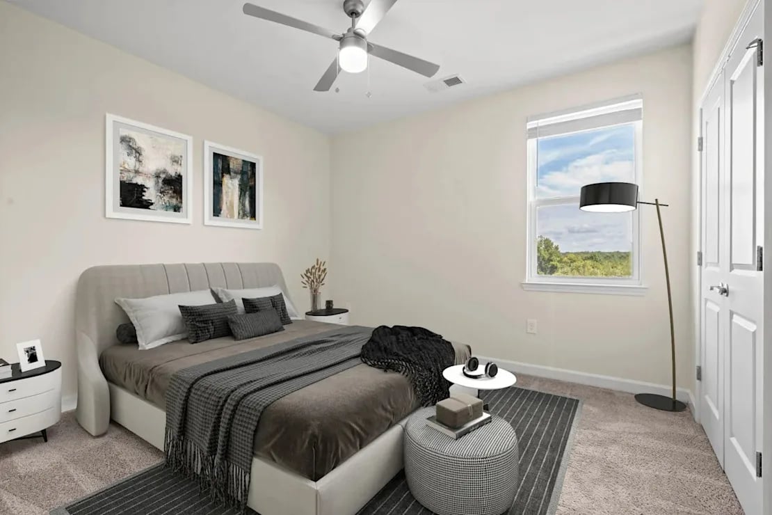 Modern bedroom with a king-sized bed, gray upholstered headboard, striped gray blankets, two framed abstract paintings, and a floor lamp near a window showing trees outside.