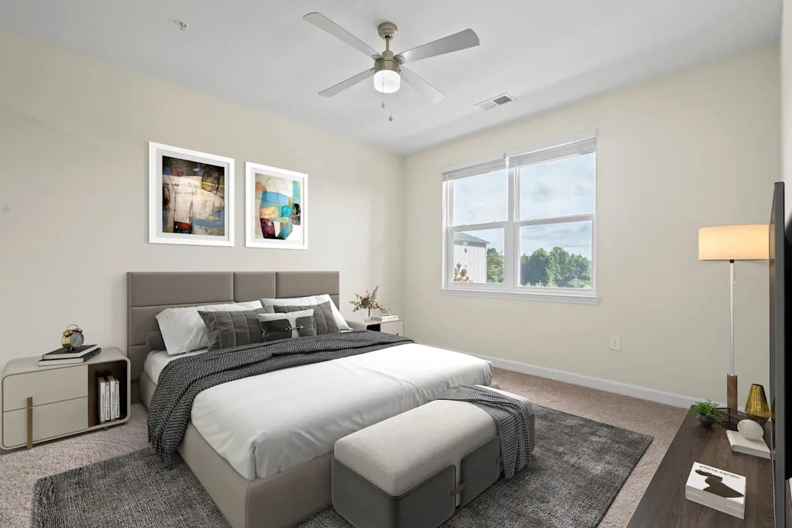 Modern bedroom with a large bed featuring a gray padded headboard, multiple pillows, and a gray throw blanket, flanked by two nightstands, a ceiling fan, and a window showing greenery outside.