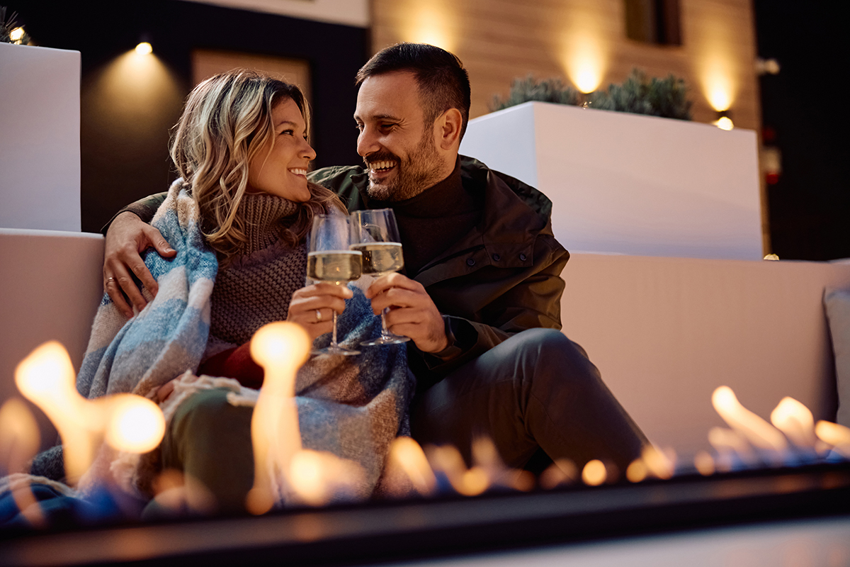 Couple sitting on a rock overlooking green hills and a sunset with cloudy sky.