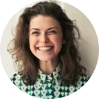 Smiling woman with curly brown hair wearing a green and white patterned blouse.