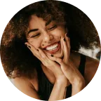 Smiling woman with curly hair resting her face in her hands.