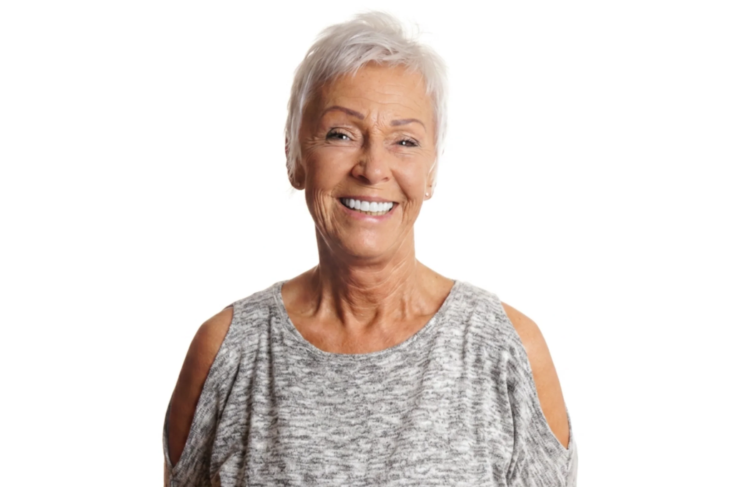Smiling older woman with short white hair wearing a gray cold-shoulder top against white background.